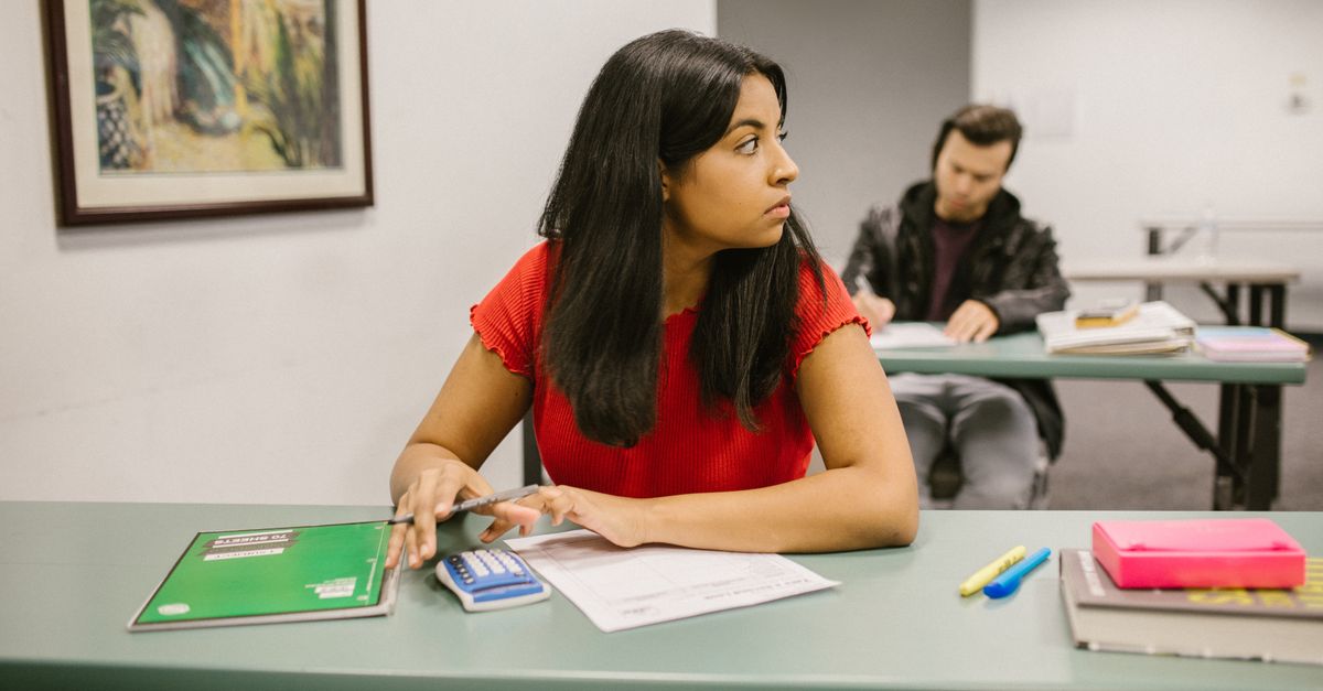 Students taking a test in a classroom, with one woman looking sideways. Education theme.